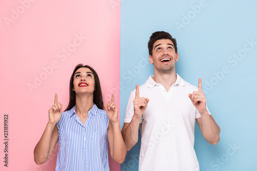 Image of happy couple in casual wear smiling and gesturing fingers upward, isolated over colorful background