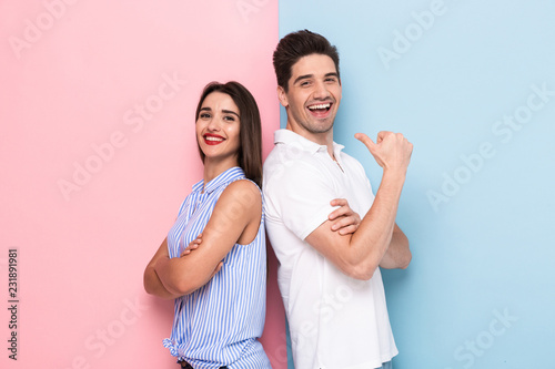 Image of young man and woman in casual wear standing back to back with arms crossed, isolated over colorful background photo