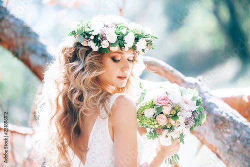 beautiful bride in nature in a coniferous forest in a wreath on her head and a luxurious wedding dress