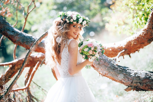 beautiful bride in nature in a coniferous forest in a wreath on her head and a luxurious wedding dress