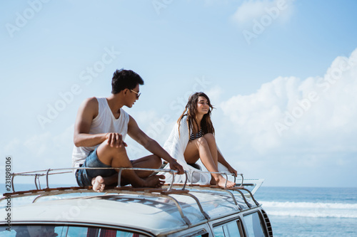 young couple with sunglasses sitting on top of minivan roof © Odua Images