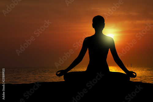 Silhouette of woman practicing yoga on the beach at sunset