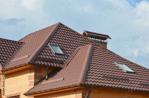 Roofing construction with metal roof, attic skylight windows, rain gutter pipes, chimney, roof protection from snow. Modern house metal roof warproofing problem area.