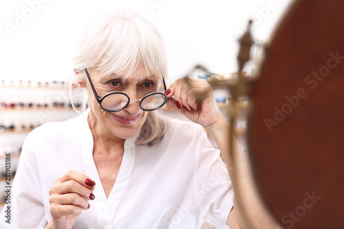 Dojrzała kobieta wada wzroku osób starszych. Starsza kobieta w salonie optycznym dobiera oprawki okularowe.