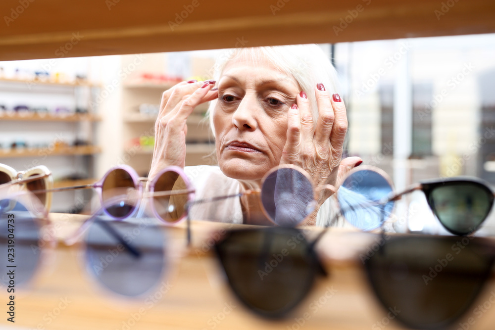 Starsza kobieta kupuje okulary przeciwsłoneczne - obrazy, fototapety, plakaty 