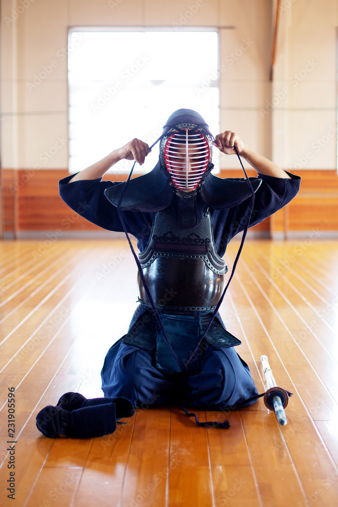 Female Japanese Kendo fighter kneeling on wooden floor, fastening