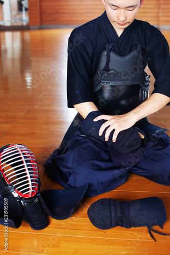Male Japanese Kendo fighter kneeling on wooden floor, putting on Kote, hand protectors. photo