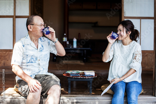 Japanese man and woman sitting on floor on porch of traditional Japanese house, drinking tea. photo