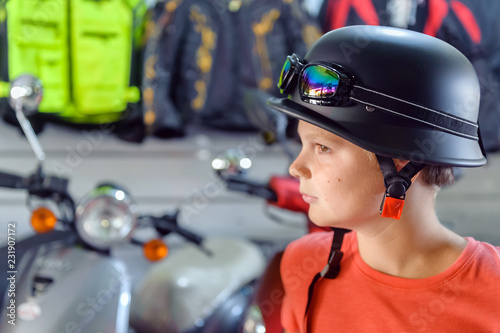 boy - teenager measures vintage motorcycle helmet and glassesin a motorcycle store. profile portrait photo