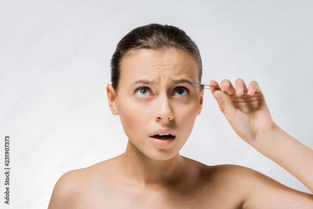 young confused woman holding metal tweezers near face young confused woman holding metal tweezers near face