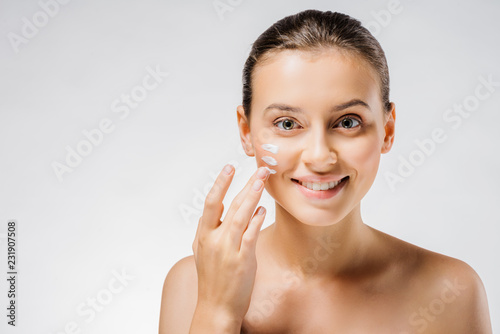 young beautiful woman applying white cream with fingers on cheek photo