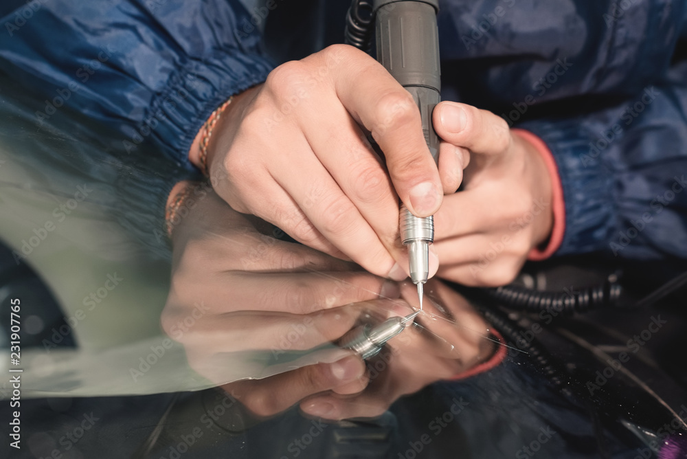 Close up Car glaze worker fixing and repairing a windshield or windshield of a car at a garage service station. Drill glass for repair Close up Car glaze worker fixing and repairing a windshield or windshield of a car at a garage service station. Drill glass for repair