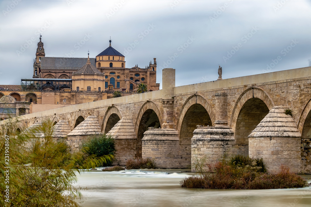 Long exposure photography of Mosque-Cathedral and the Roman Bridge in Cordoba with cloudy sky, Andalusia, Spain