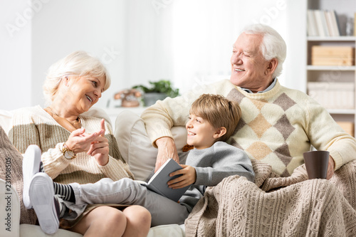 Grandmother and grandfather siting on couch with their grandson, reading a book