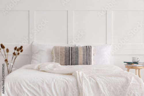 Patterned pillow on the king size bed in white simple bedroom interior in elegant apartment, real photo