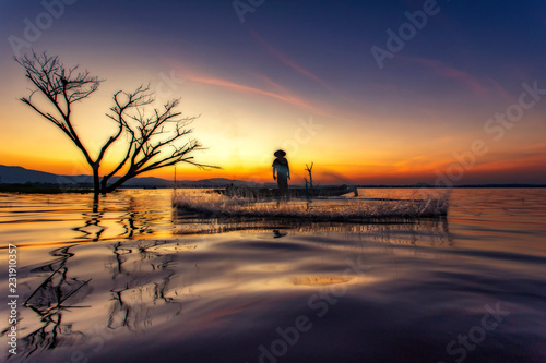  Fishermen throwing net fishing onthe Boat in sunrise time at the Lake inside dead tree © uaychai