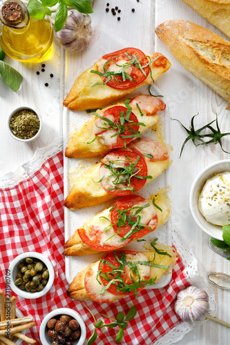 Bruschetta, grilled slices of baguette with mozzarella cheese, tomatoes, garlic and aromatic basil on a white wooden table, top view. A delicious Mediterranean appetizer