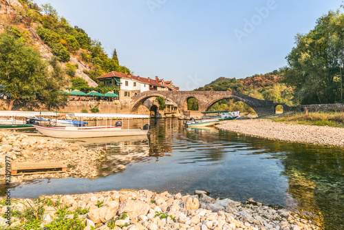 Old arched stone bridge across the river Crnojević, Montenegro. Boat pier and hotel at the source of the river.