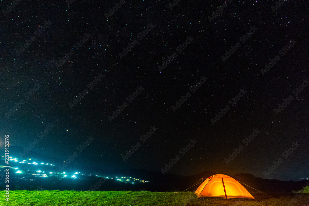 Orange tent glows under night sky.