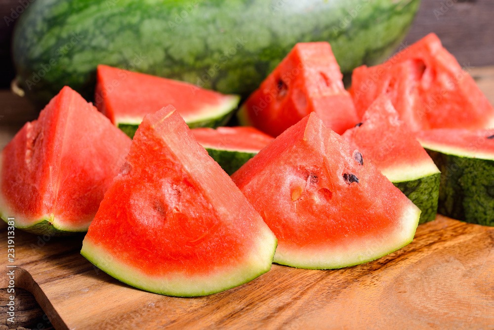 whole and portion cut watermelon on wooden cutting board