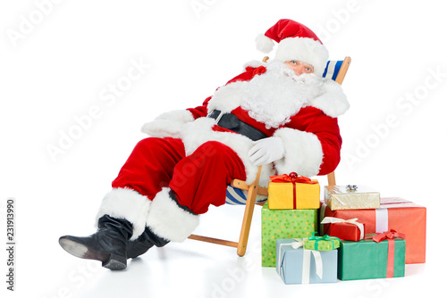 santa claus relaxing on beach chair with christmas presents on white © LIGHTFIELD STUDIOS