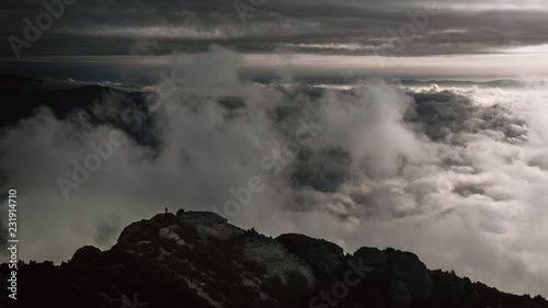 Una persona en la cima de una montaña con las nubes detrás. 