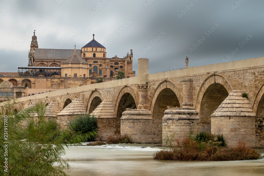 Long exposure photography of Mosque-Cathedral and the Roman Bridge in Cordoba with cloudy sky, Andalusia, Spain