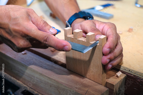 Skilled joiner working in carpentry. Amateur woodworker making dovetail join for wooden drawer in carpenters workshop