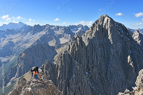 Female climber with helmet and backpack climbing in a wild rocky landscape with steep mountains under blue sky at a beautiful day in autumn. Dremelspitze, Lechtal Alps, Tyrol, Austria.