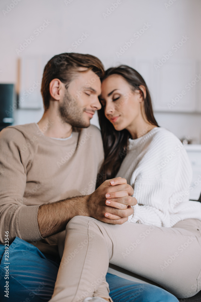 happy young couple cuddling and holding hands on couch at home happy young couple cuddling and holding hands on couch at home