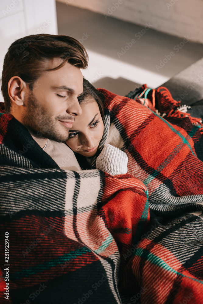 Fototapeta premium high angle view of happy young couple relaxing on couch and covering with plaid