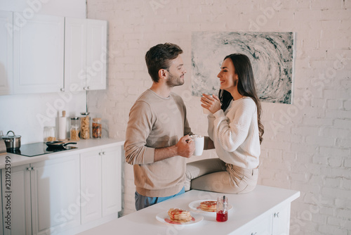 smiling young couple having breakfast together and chatting at home