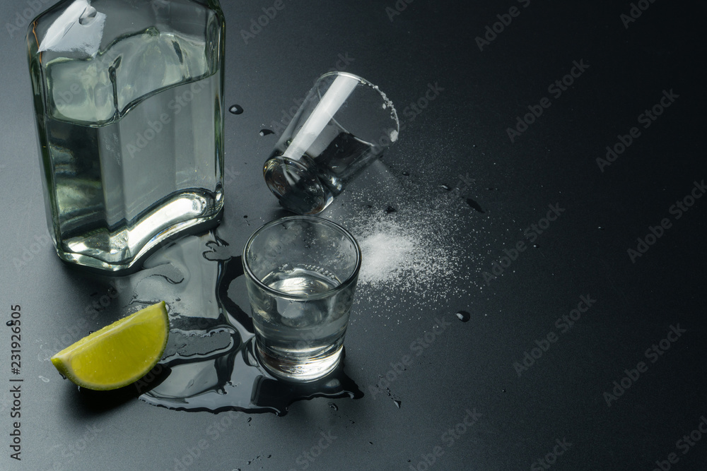 Fototapeta premium a bottle of silver tequila with the tequila shot glasses and the lime slice with salt on the wet table