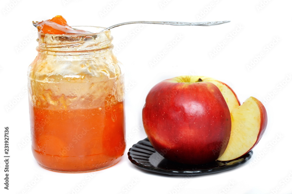 Open glass jar with natural orange sweet fruit jam on which lies a teaspoon and an incised red ripe Apple on a white background. Isolated Open glass jar with natural orange sweet fruit jam on which lies a teaspoon and an incised red ripe Apple on a white background. Isolated