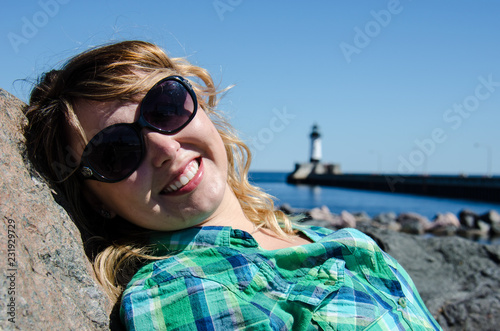 Portrait of a young adult woman leaning on rocks at Canal Park in Duluth Minnesota. Lighthouse blurred in background