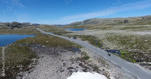 Norwegian Scenic Route Aurlandsfjellet. Motorcycle drives past stopped car in highlands with stunning landscapes. Aerial view from flying drone. Norway