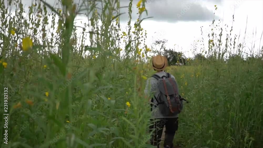 Happy and joyful tourist backpacker with hat and bag excitedly walking and jumping on the countryside grassland Happy and joyful tourist backpacker with hat and bag excitedly walking and jumping on the countryside grassland