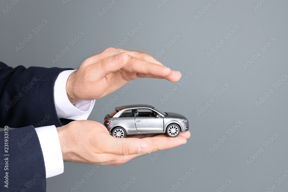 Male insurance agent holding toy car on grey background, closeup. Space for text Male insurance agent holding toy car on grey background, closeup. Space for text