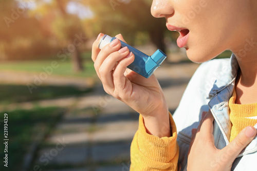 Woman using asthma inhaler outdoors. Space for text photo