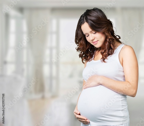 Pregnant young woman in white t shirt on bright background