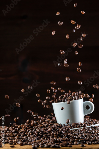 Fotografija Roasted coffee beans falling down on white cup on wooden table