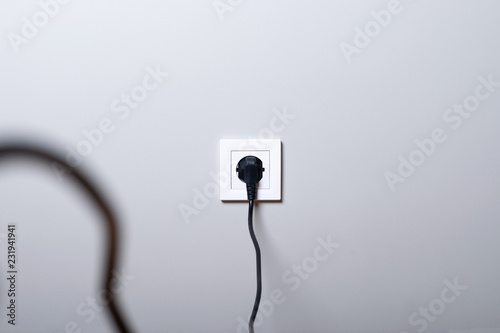 Electric white socket and one plugged in power cord on white wall background