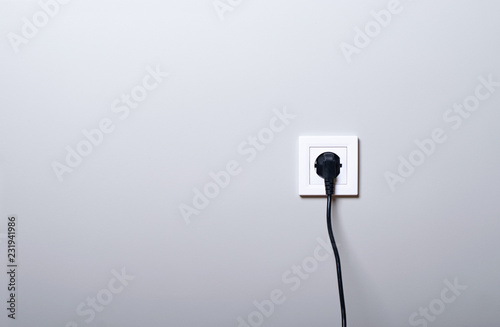 Electric white socket and one plugged in power cord on white wall background