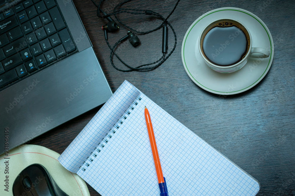 a clean notebook on the desktop, next to the laptop, a cup of coffee, headphones. A place to create ideas a clean notebook on the desktop, next to the laptop, a cup of coffee, headphones. A place to create ideas