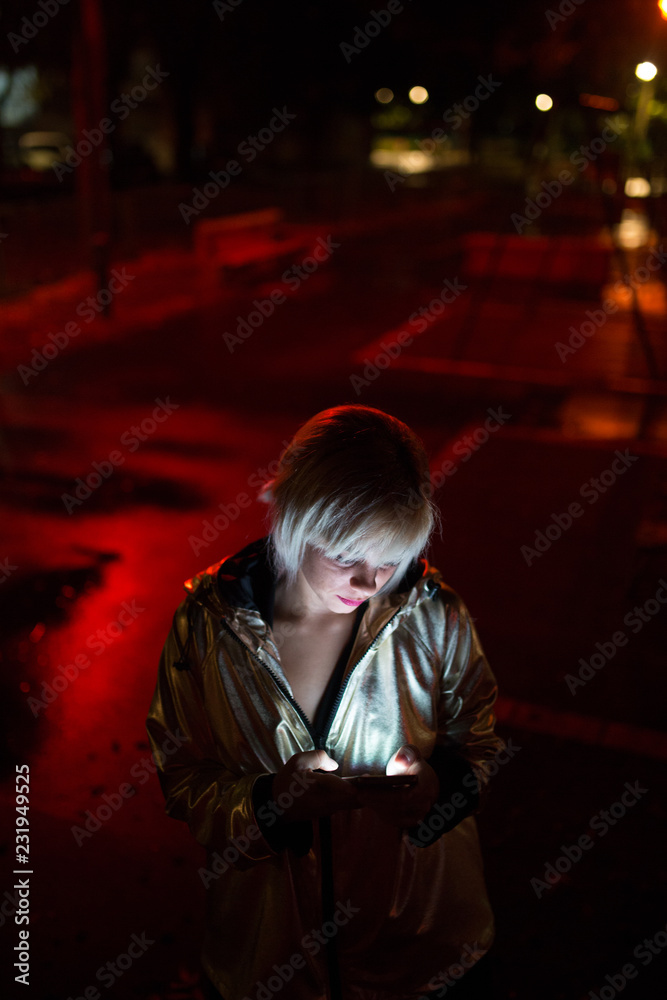Woman in silver jacket using her phone lit by red light Woman in silver jacket using her phone lit by red light