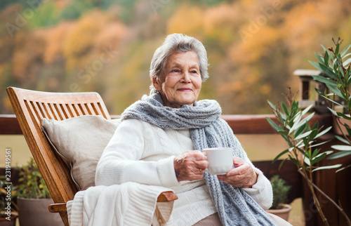Obraz na plátně An elderly woman sitting outdoors on a terrace in on a sunny day in autumn