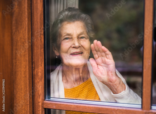 An elderly woman standing by the window, looking out. Shot through glass.