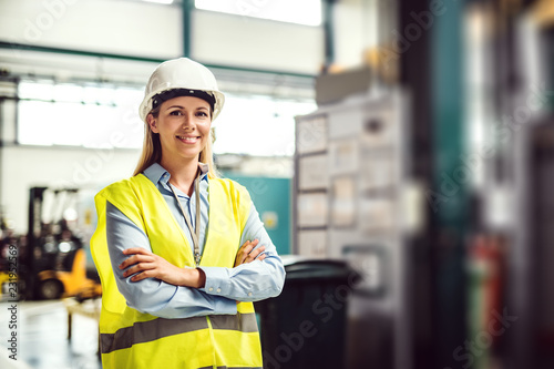 A portrait of an industrial woman engineer standing in a factory, arms crossed.