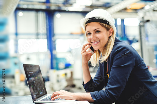 A portrait of an industrial woman engineer in a factory using laptop and smartphone. photo