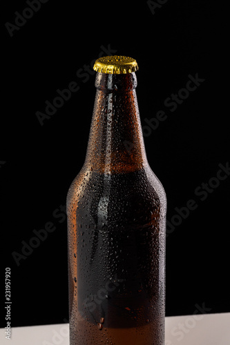 Bottle with soft drinks or alcohol in the ice. On gold caps and a bottle neck are drops of dew. Beer bottle cap close-up macro on black background with clipping path.
